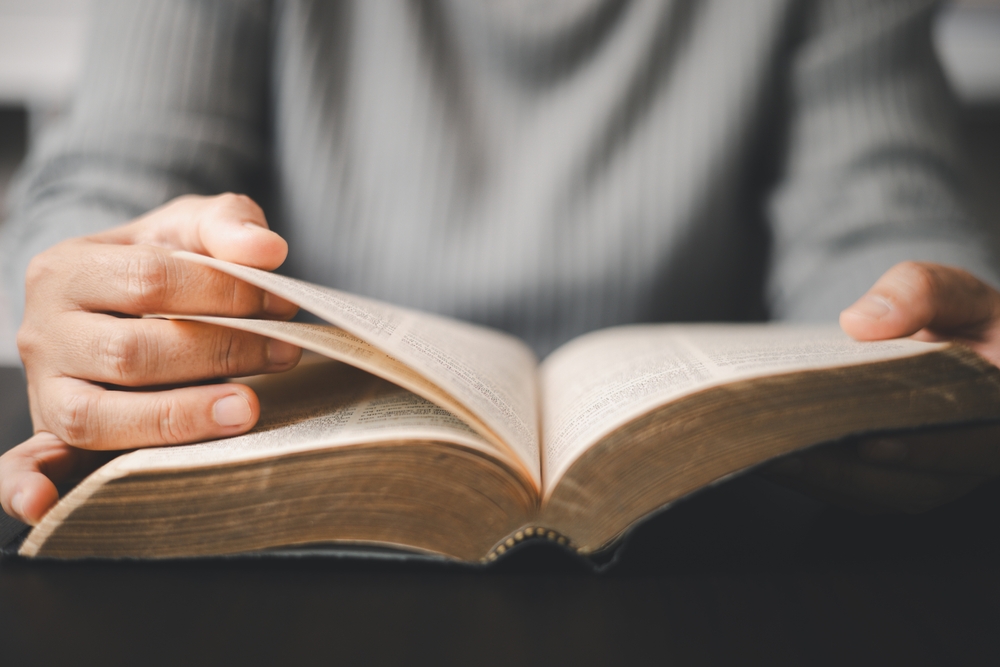 Christian woman reading bible in ancient Catholic temple. Devout Christian woman engages in prayer, fervently reading her Bible against religious background, embodying essence of Catholic devotion.