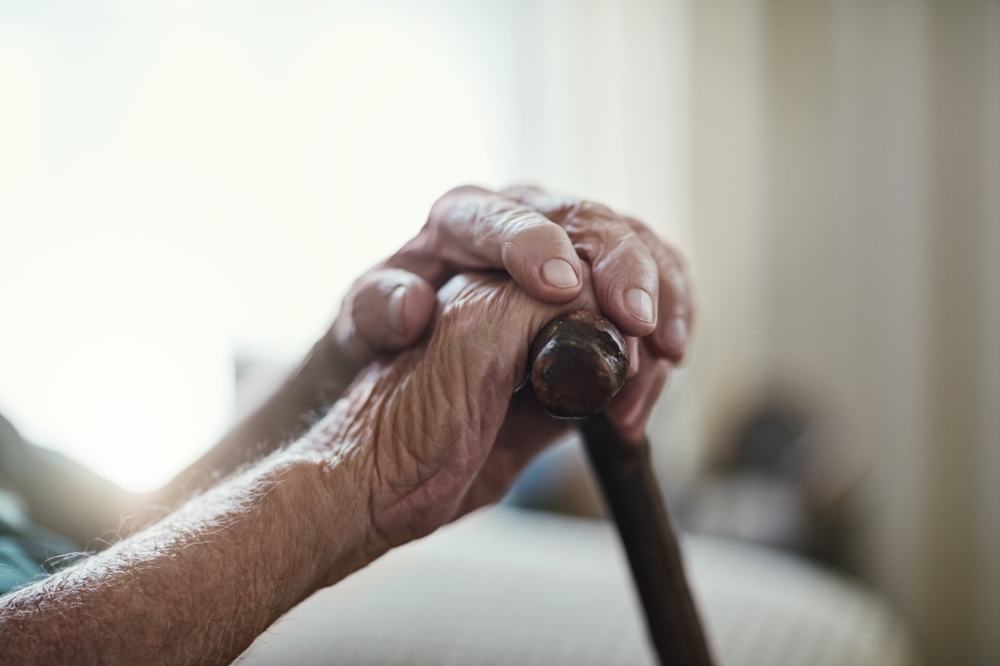 Senior man, hands together and support with cane for old age, osteoporosis or care in retirement home. Closeup of elderly, pensioner or male person with a disability or walking stick for stability
