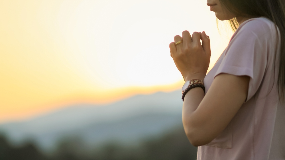 young woman clasped her hands together in prayer asking for forgiveness from God based on her Christian beliefs and faith in God teachings. concept prayer and intercession according beliefs about God