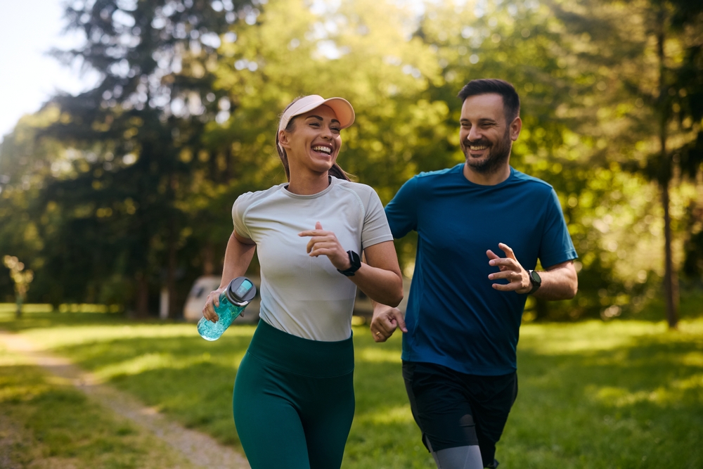Happy athletic couple having fun while running together in nature. Copy space.
