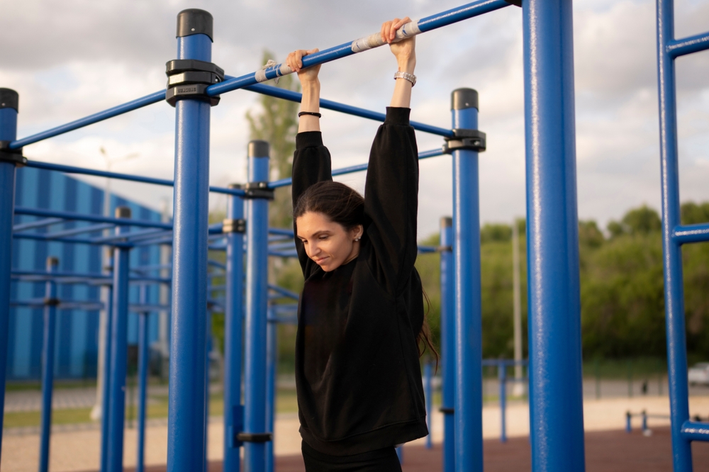Young Female Athlete Hanging on the Bar on Outdoor Exercise Equipment