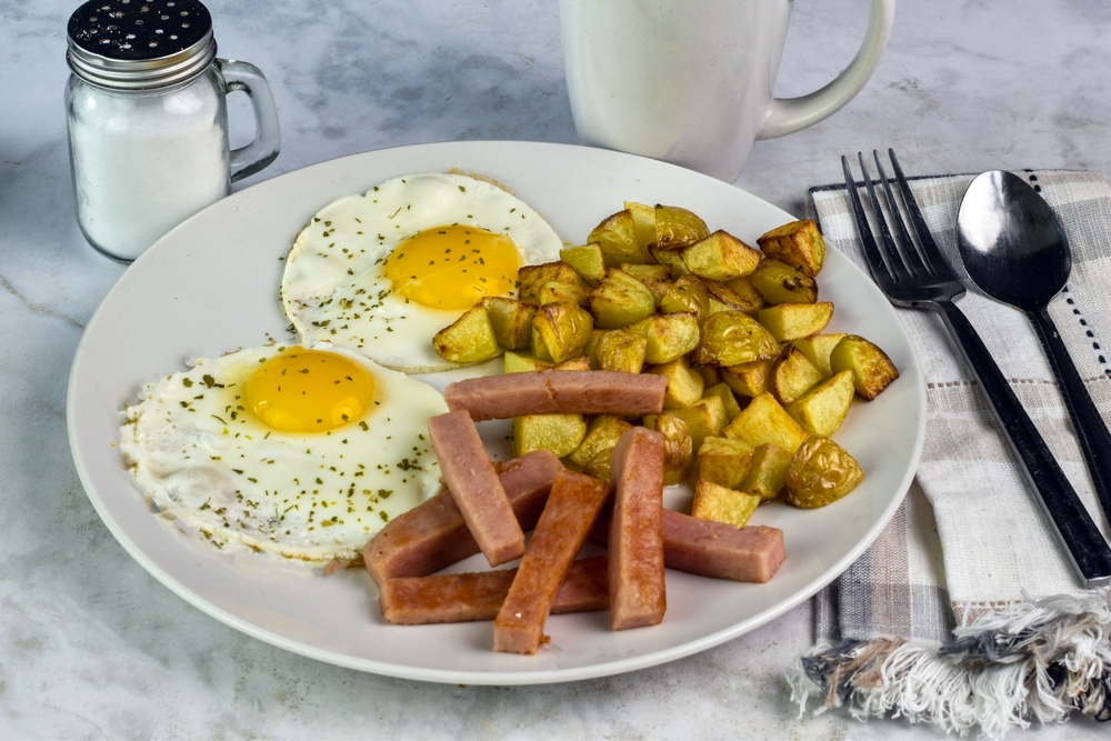 fried eggs top with parsley served with lightly cook spam sticks and home fries,
