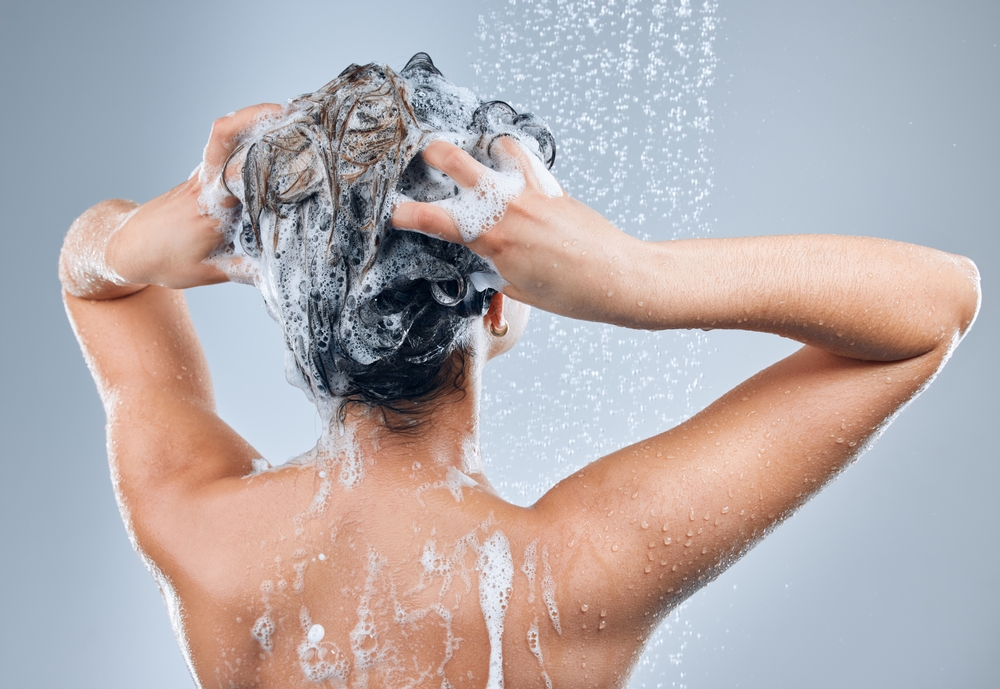 Shower water, hair care and back of woman for hygiene, shine results and clean scalp for growth in studio. Liquid drops, model girl and foam wash for texture and cleaning routine by grey background