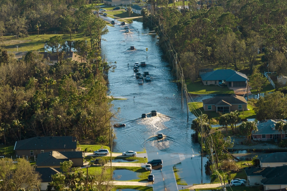 Hurricane flooded street with moving cars and surrounded with water houses in Florida residential area. Consequences of natural disaster
