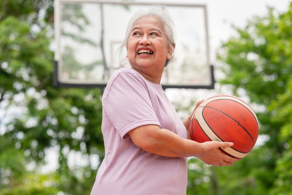 Cheerful active senior woman playing basketball in the urban outdoor basketball court, healthy life concepts
