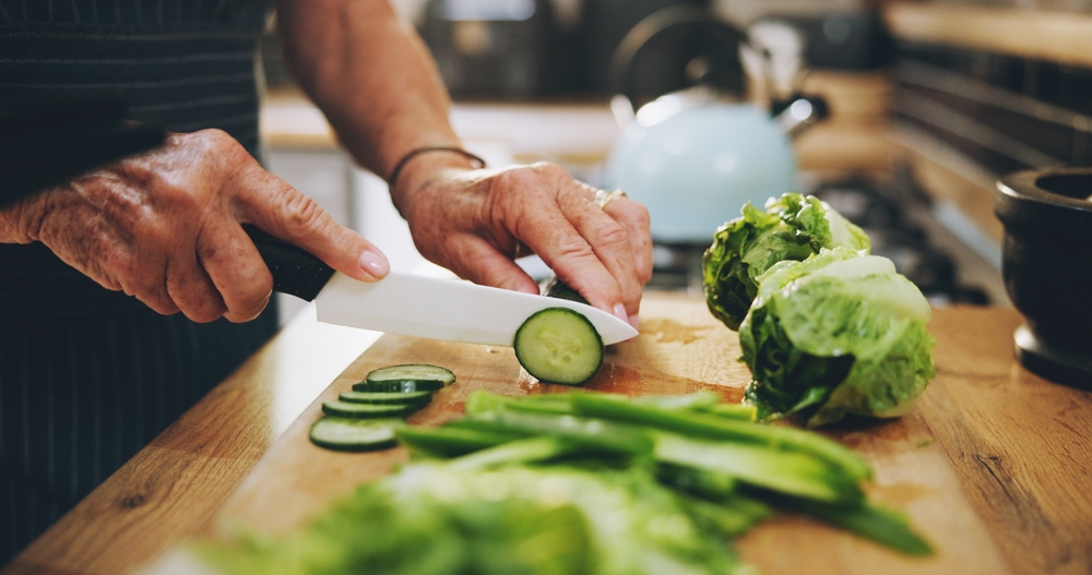 Hands, cutting board and salad in kitchen with green vegetables for healthy food or nutrition. Person with culinary skills for cooking lunch with lettuce, cucumber and organic ingredients at home
