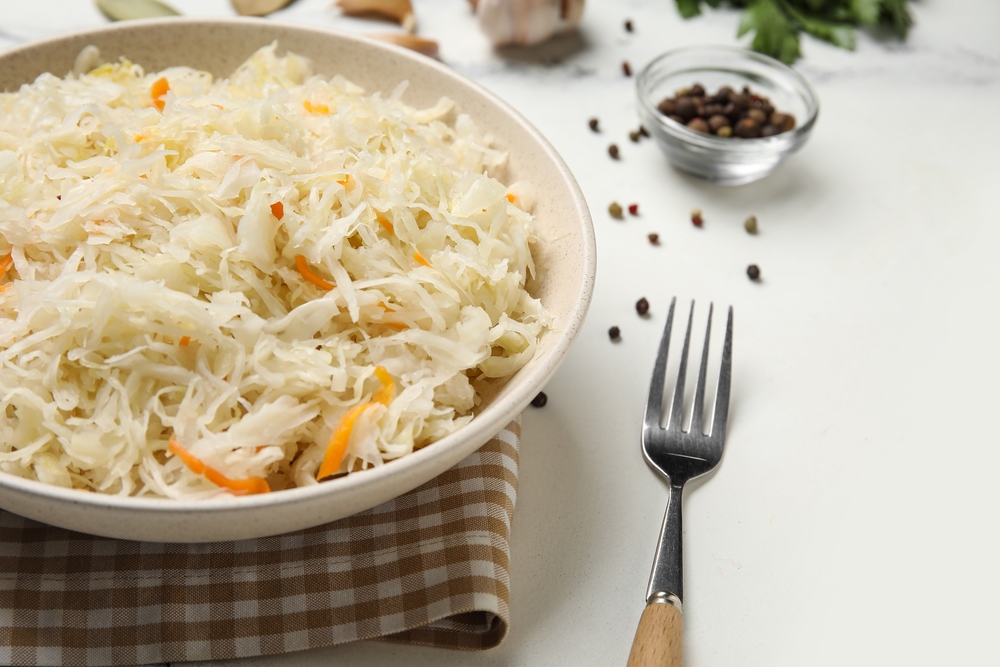 Bowl with delicious sauerkraut and peppercorn on white background
