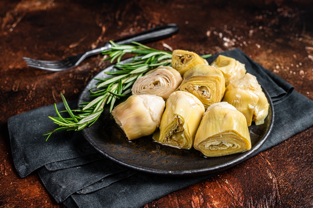 Italian appetizer Artichoke hearts pickled in olive oil with herbs and spices Dark background. Top view.