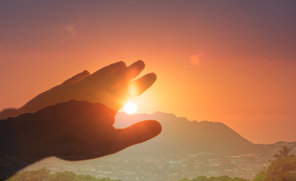 Persons hand in nature reaching out to touch the warm sun light. Spiritual, light, healing energy concept