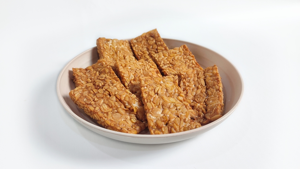 Closed up of Fried Tempeh or Tempe Goreng on white plate. Isolated on white background with copy space. Traditional Indonesian food made from fermented soybeans. Clipping path