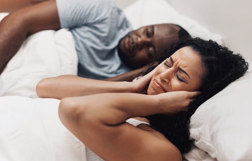 Angry, snoring and couple in bed with sleep apnea frustrated by husband with noise, problem and upset woman. Exhausted, cover ears and tired man asleep with fatigue, sinus allergy and burnout in home
