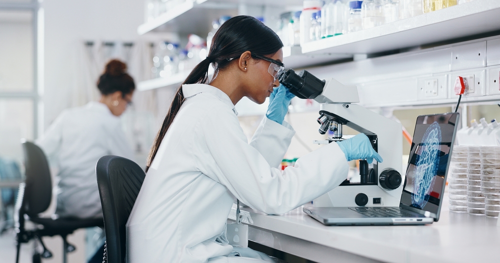 Laptop, research and woman with microscope, science and check experiment for cancer treatment. Person, scientist and employee with lab equipment, vaccine and cure development with dna and bacteria
