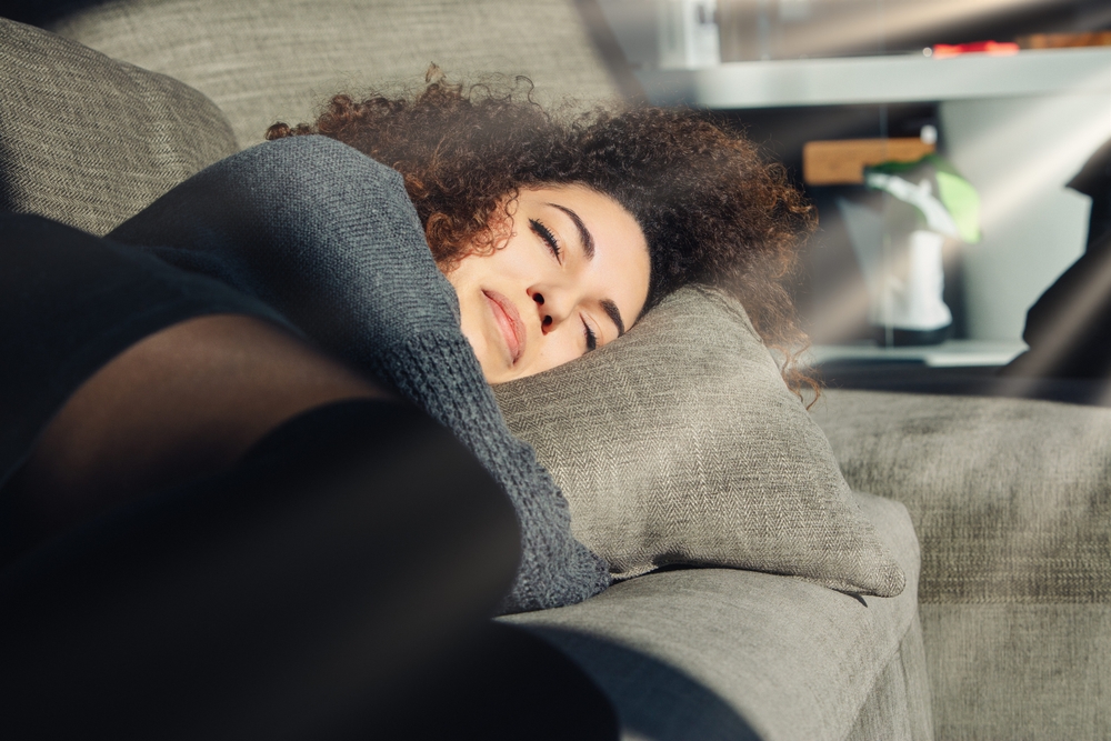 Young woman is taking a nap on a comfortable sofa in the afternoon sun, enjoying a moment of peace and quiet in her living room
