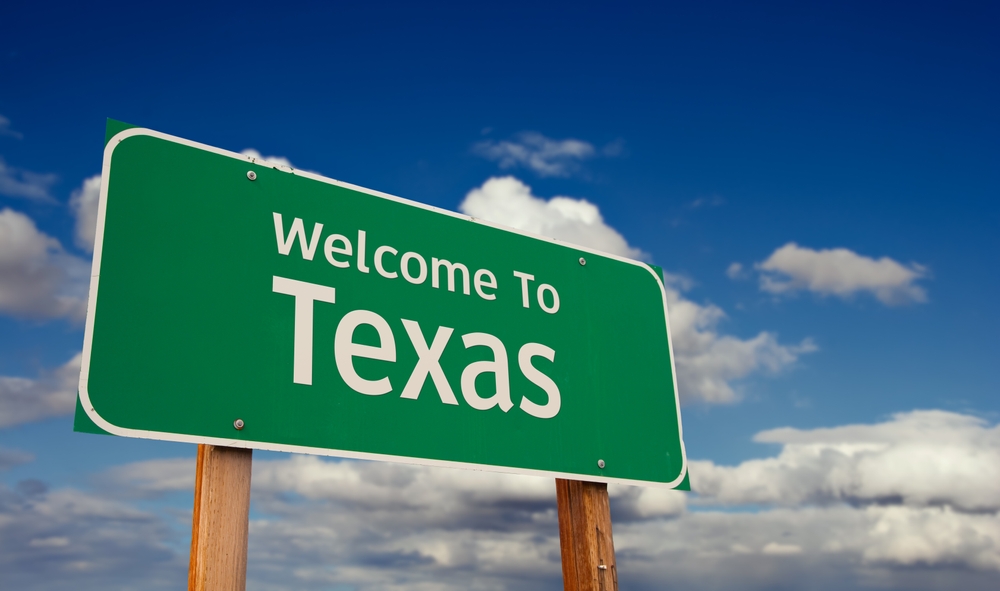 Welcome To Texas Green Road Sign Over Blue Sky with Some Clouds.
