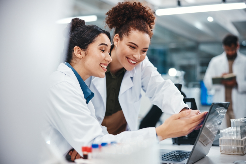 Laptop, scientist and women with smile, medical research and excited for results of test and pointing. Lab, online and conversation for medicine of healthcare, pharmaceutical and collaboration
