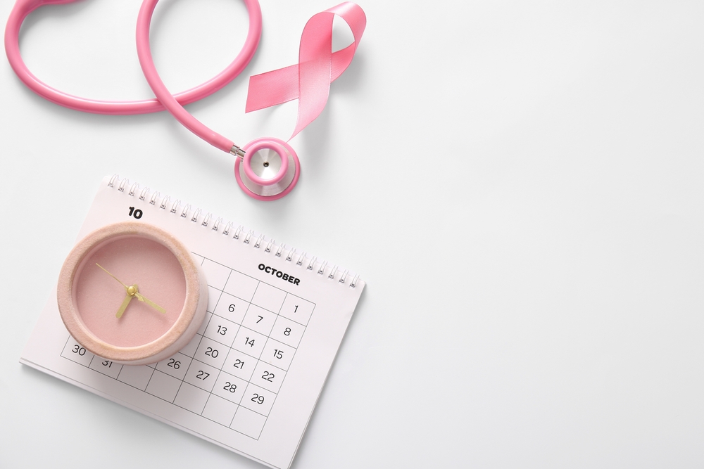 Pink ribbon, alarm clock, calendar and stethoscope on light background. Breast cancer awareness concept