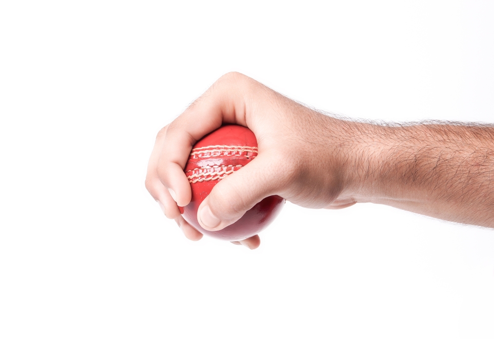Closeup Photo Of A Male Bowler Firmly Gripping On A Red Test Match Cricket Ball On White Background