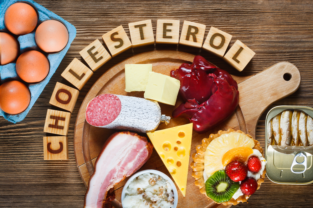 Foods rich in cholesterol as eggs, liver, yellow cheese, butter, bacon, lard with onion, sardines in oil and sweet dessert - cupcake with cream. Wooden table as background
