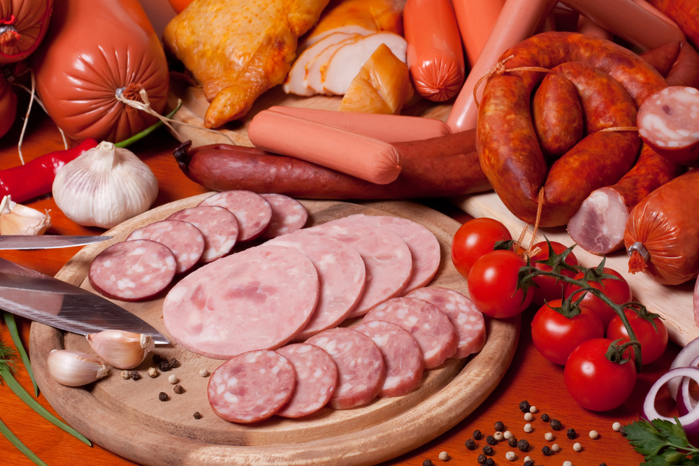 A variety of processed cold meat products, on a wooden cutting board.
