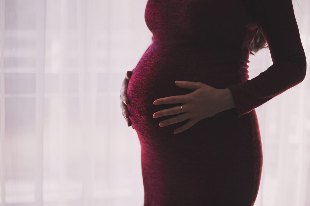 A pregnant woman holding her belly and wearing a red dress. White background.