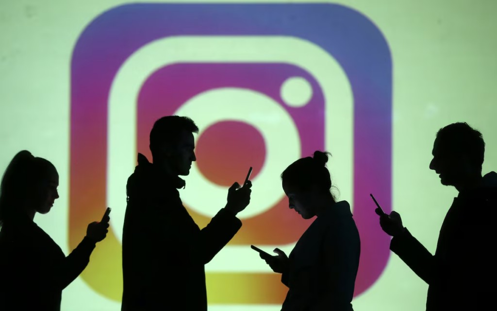 Silhouettes of mobile users are seen next to a screen projection of Instagram logo in this picture illustration taken March 28, 2018.