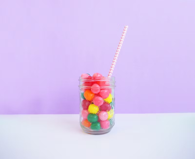 a mason jar full of candy with a straw sticking out