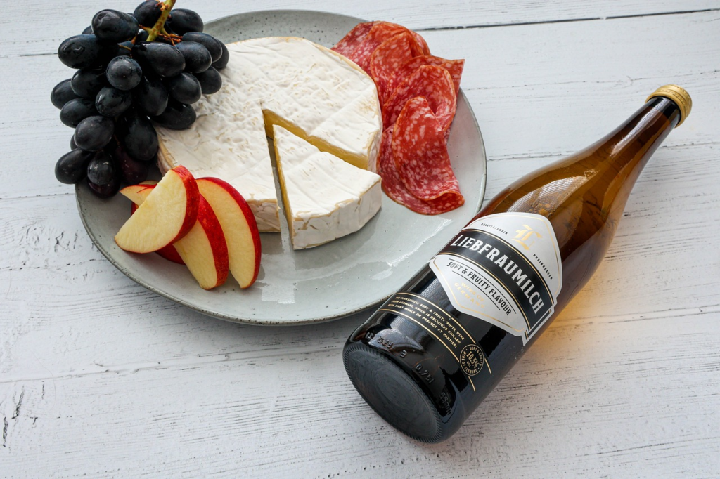 Brie cheese on a plate with apple slices, grapes, salami, and wine. White wooden background.