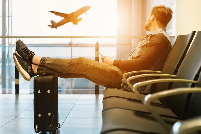 man in an airport seat looking out at a plane taking off