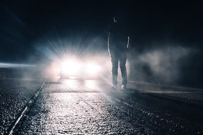 a car's headlights shining on a man on the road