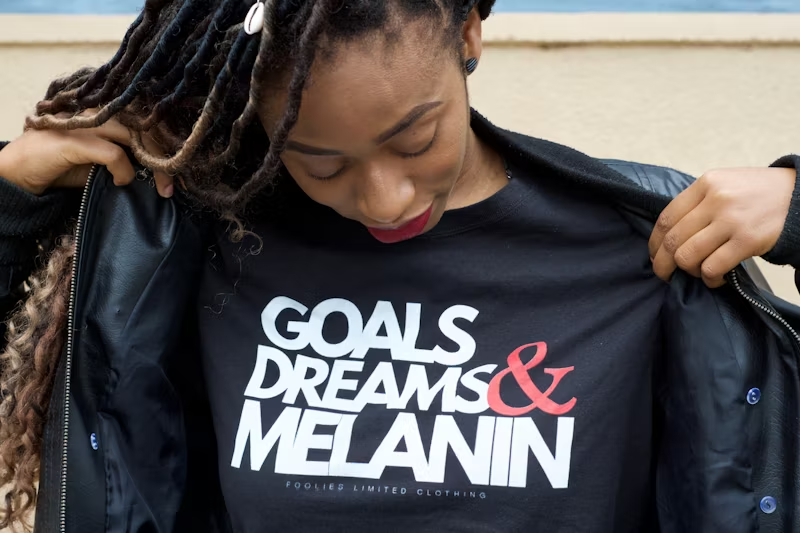 a woman wearing a shirt saying 'Goals Dreams & Melanin'