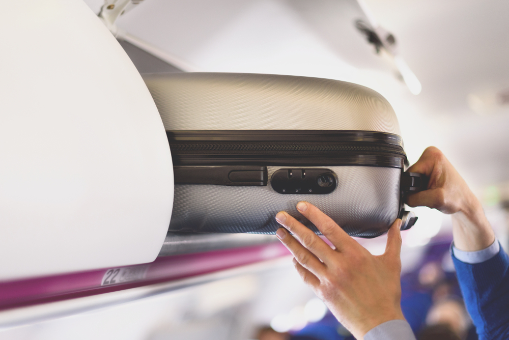 Hand-luggage compartment with suitcases in airplane. Hands take off hand luggage. Passenger put cabin bag cabin on the top shelf. Travel concept with copy space