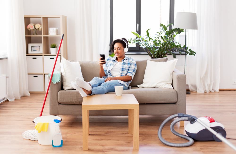 household and technology concept - happy african american woman or housewife in headphones with smartphone resting after home cleaning, listening to music and singing

