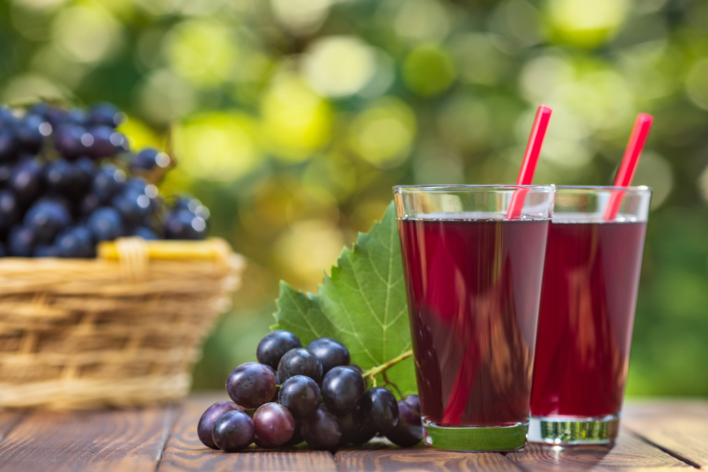 fresh grape juice in two glasses with ripe bunch of dark blue berries on wooden table outdoors