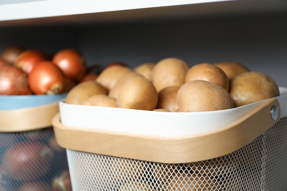 Baskets with potatoes and onions on shelf, closeup. Orderly storage
