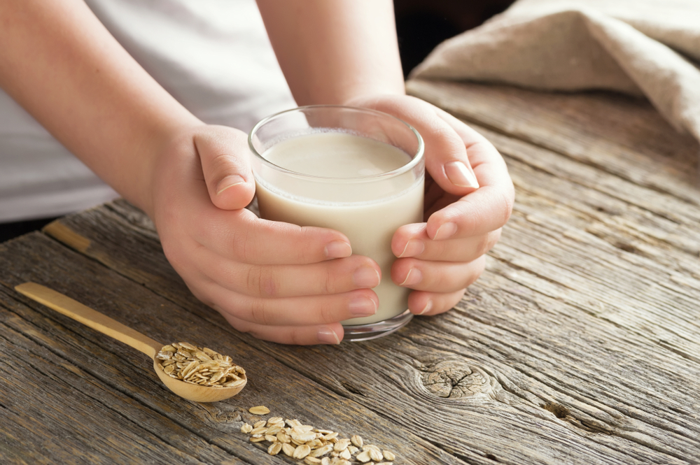 Young adult hands holds drinking glass with organic oat milk . Healthy eating lactose free milk substitute concept .Close up,selective focus.