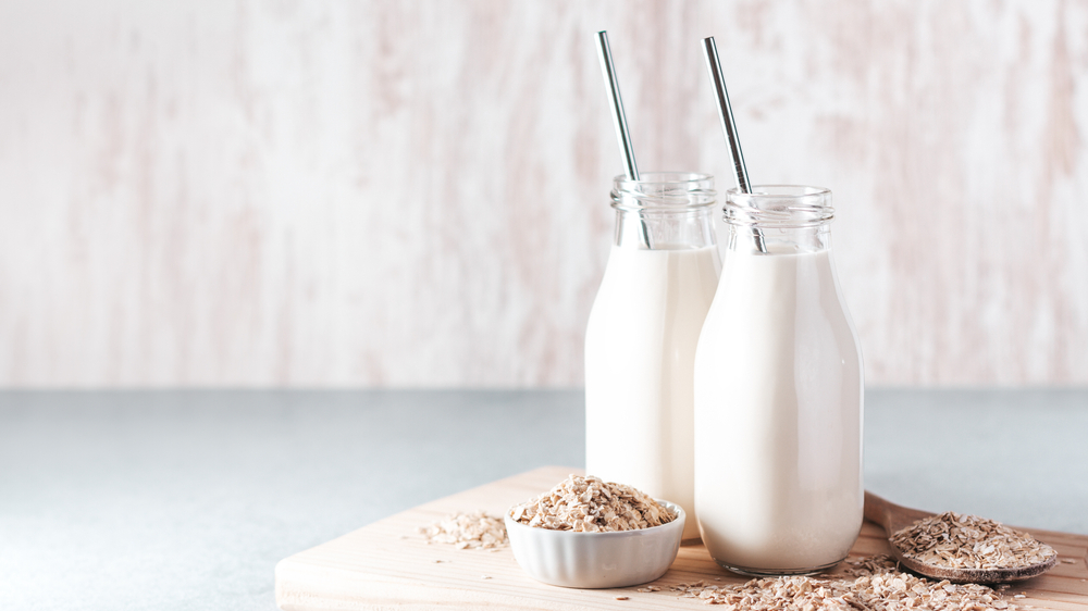 Non dairy oat milk in glass jars with reusable metal straws. Healthy vegan milk alternative still life, copy space. Substitute for traditional cow milk with oat flakes on neutral background