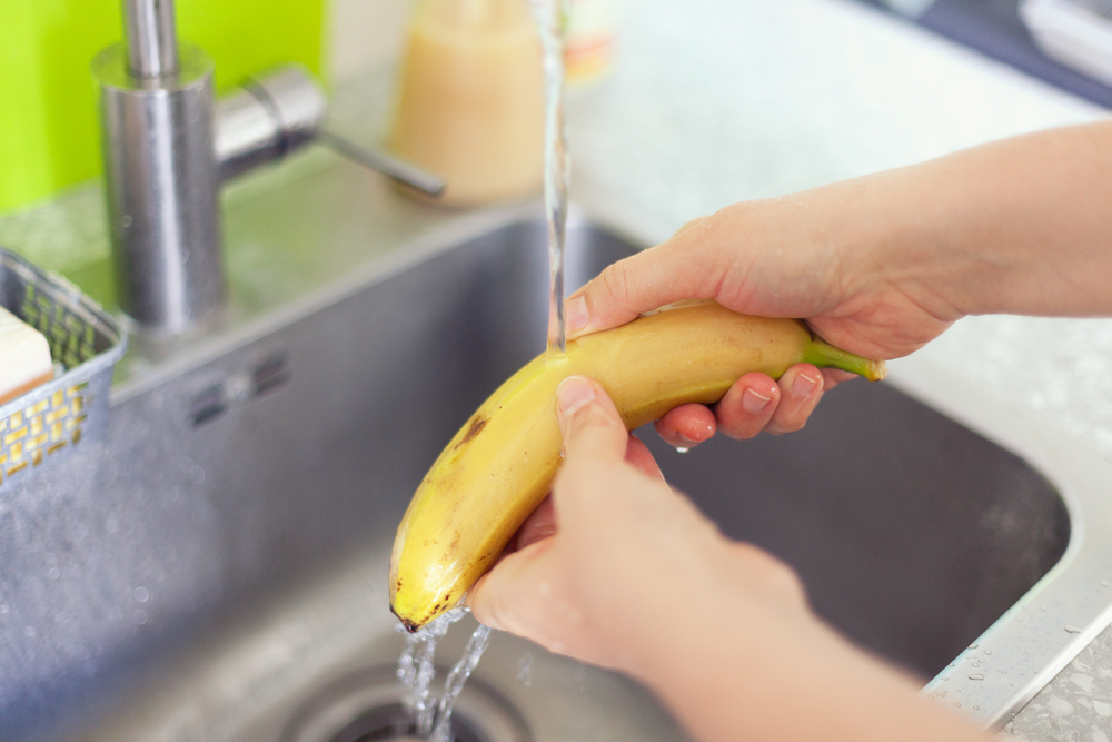 Person washing banana in a sink. Close up.