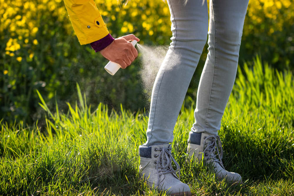 Tourist spraying insect repellent on legs and hiking boots. Protection against tick in nature