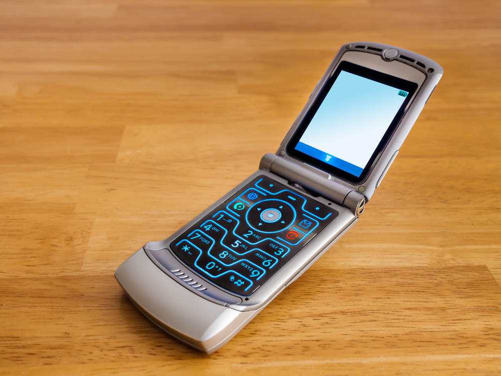 Retro flip phone cell phone. Vintage old fashioned push button mobile wireless telephone on wooden desk.
