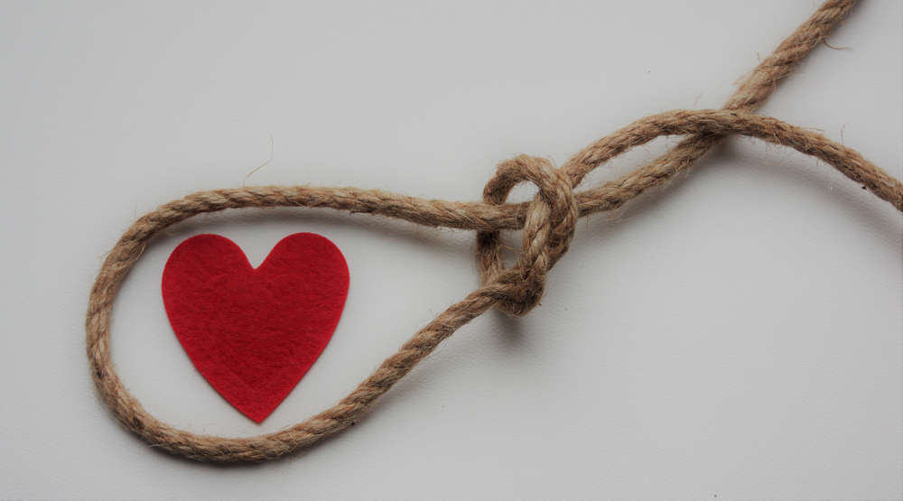 Red heart in a loop of rope cord. Feelings trap. Emotions. Toxic relations. Affection. Dependence. Abuse. Unhealthy relationship. Dysfunctional love. Manipulation. - 10 January 2021, Montreal, Canada