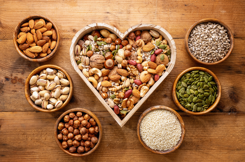 Heart shaped box and small bowls full of nuts and seed on rustic table.
