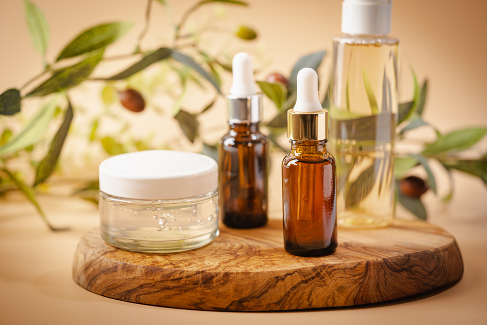 Olive based cosmetic serum, cream and water with sprig of olives on a pastel background
