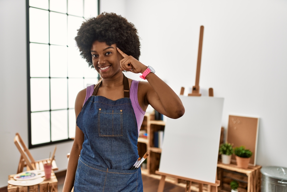 Young african american woman with afro hair at art studio smiling pointing to head with one finger, great idea or thought, good memory