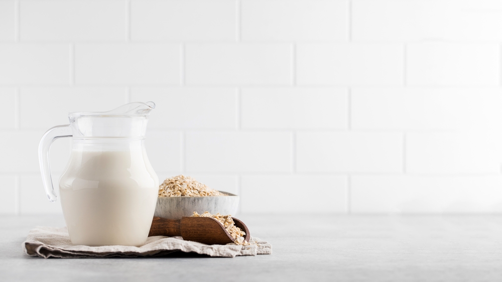 A jug of oat milk, a bowl of oatmeal on the table on a light background. Copy space.