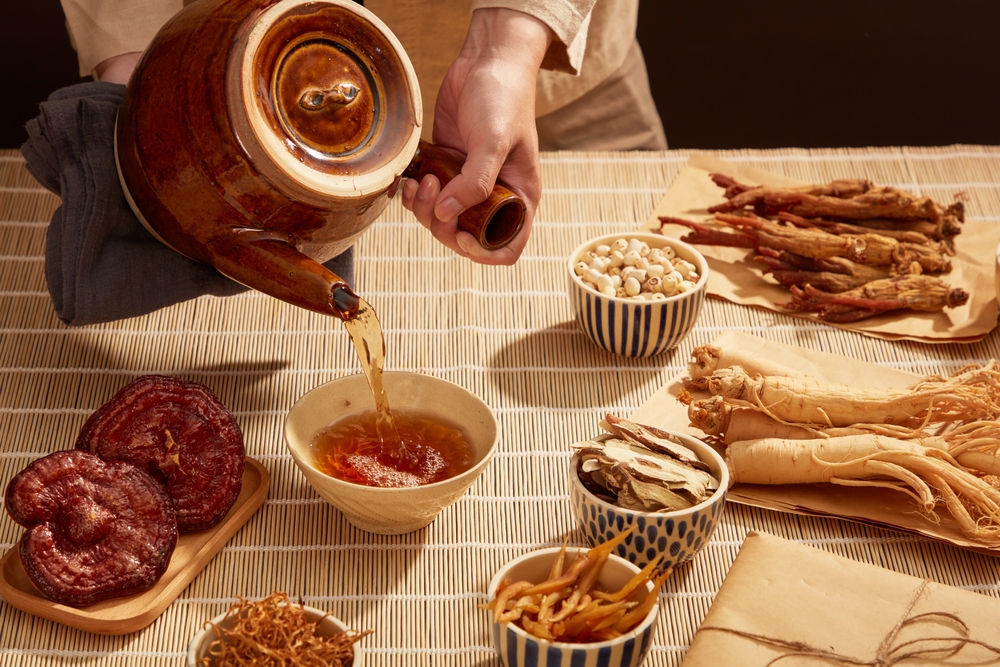 Under a bamboo mat table with a variety of natural herbs for medicine, an ancient doctor is pouring hot herbal tea.