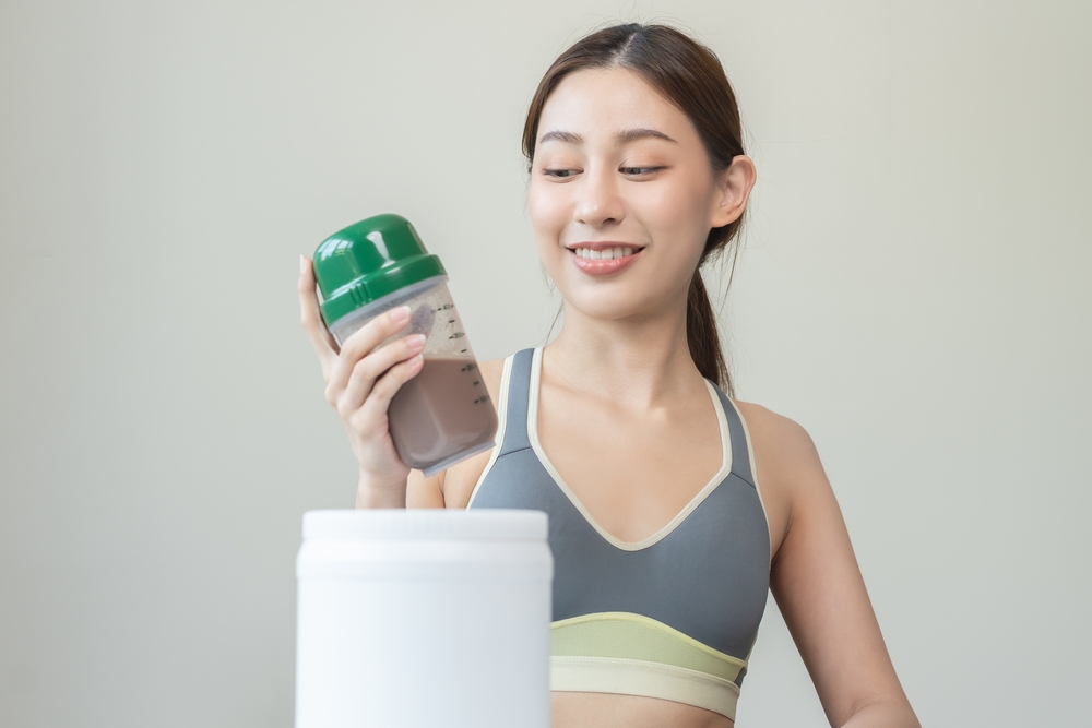 Diet meal replacement for weight loss, smile asian young woman, girl in sportswear, hand in holding protein shake bottle for drink supplement for muscle after workout at home. Healthy body care person
