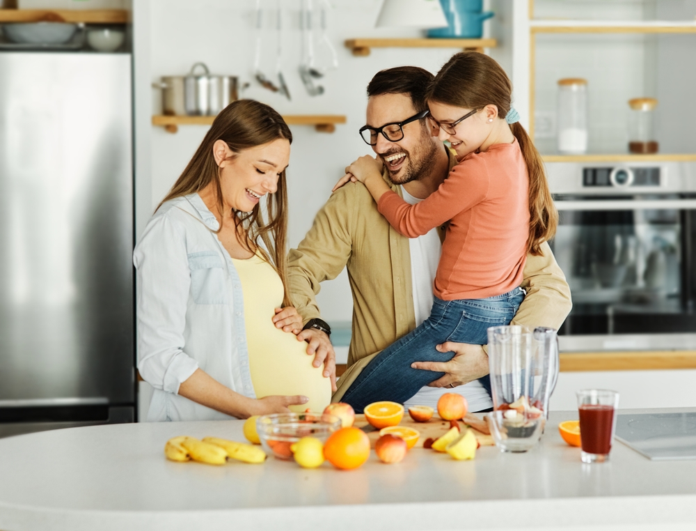Portrait of a family with a young pregnant woman preparing a healthy juice with fresh fruits in the kitchen
