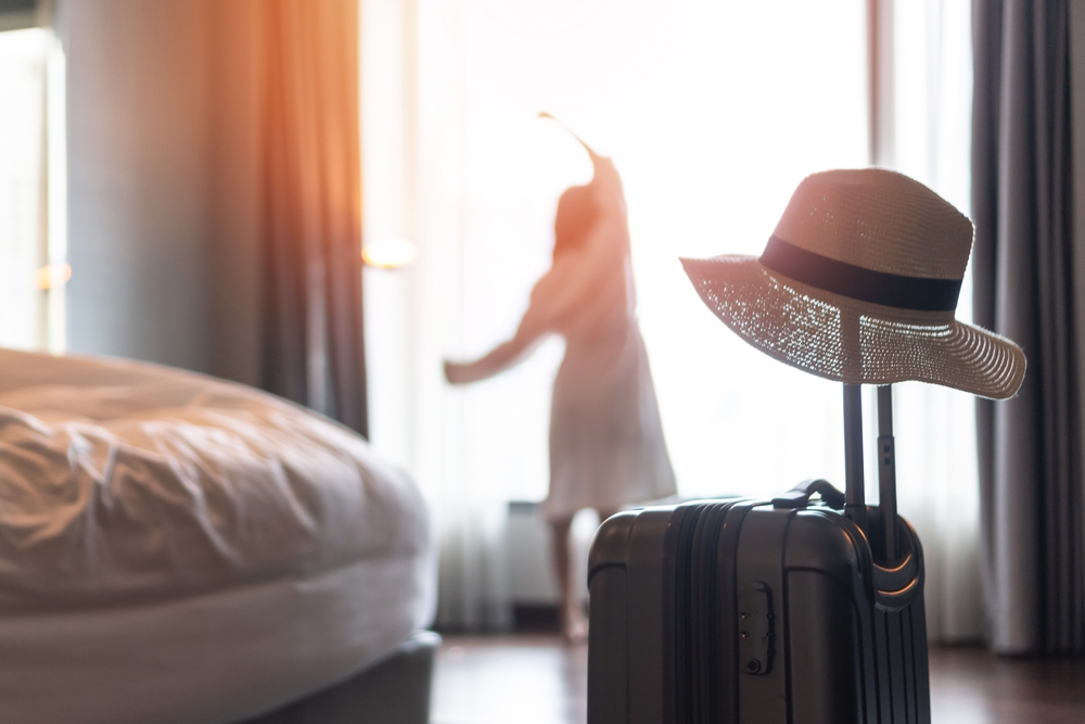Traveler woman with luggage in business hotel guest room looking out toward city view staying for work travel or vacation trip for traveler