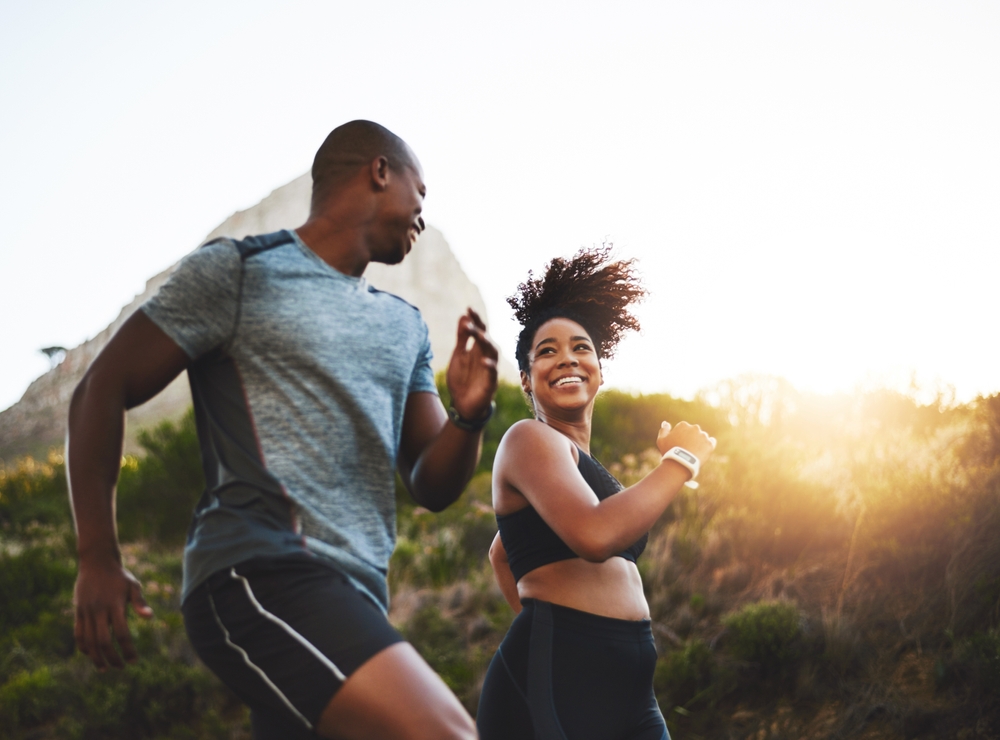 Fitness, energy and athletes running in nature by a mountain training for race, marathon or competition. Sports, health and African couple doing outdoor cardio workout or exercise together at sunset.
