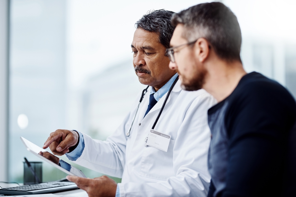 Healthcare, talking and doctor with a man and tablet for consulting, results and help with health. Planning, medicine and a mature hospital worker speaking to a patient about medical service on tech